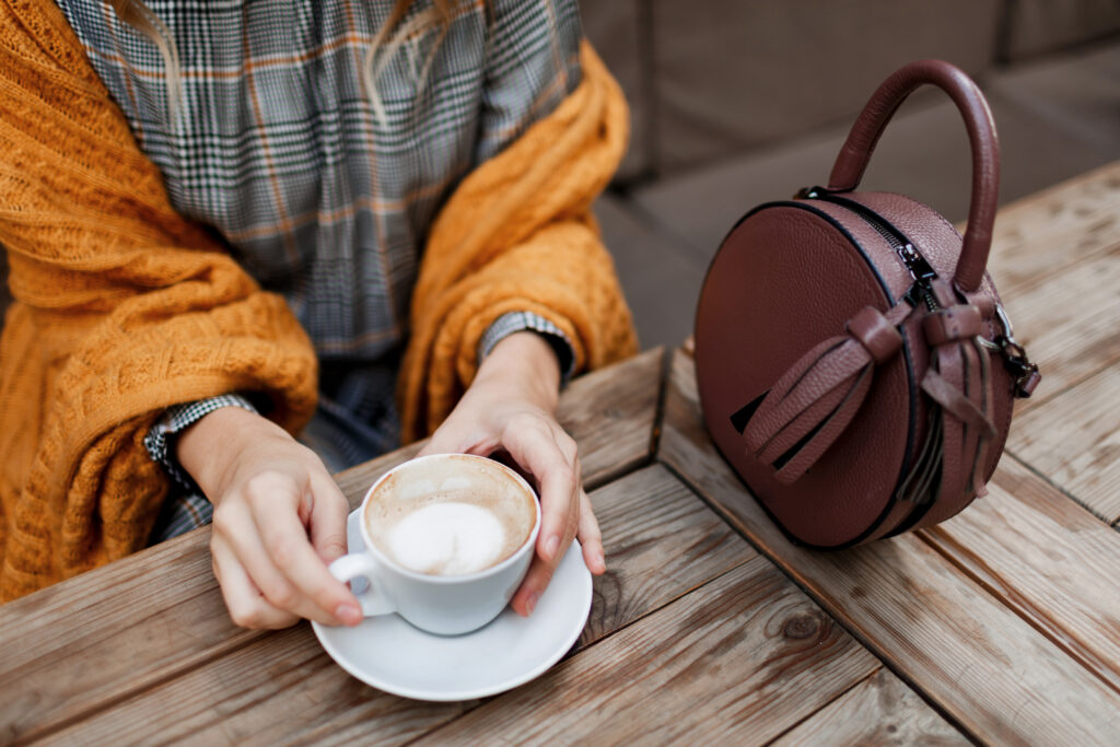 woman drinking coffee stylish bag table wearing grey dress orange plaid enjoying cozy morning cafe