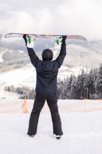 szczesliwy czlowiek stojacy z snowboard nad glowa na szczycie wzgorza gor